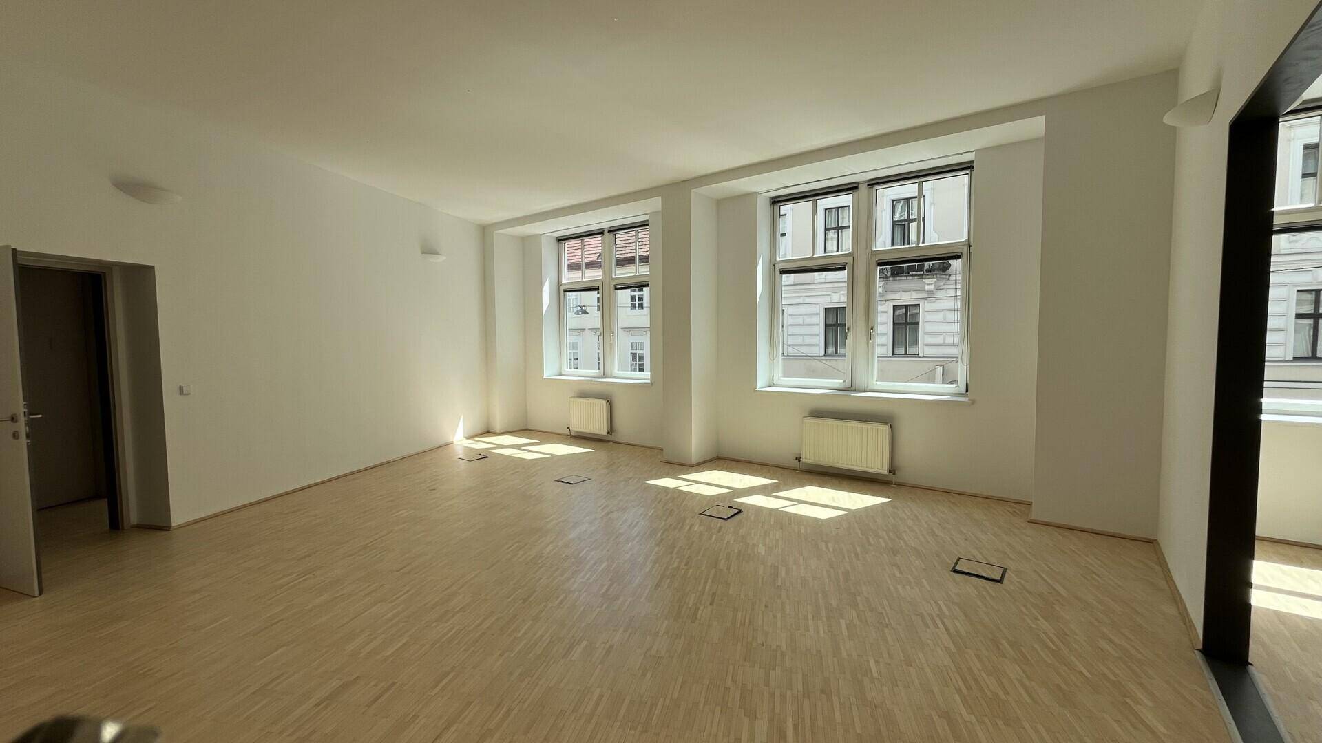 Großer, heller Büroraum mit Holzfußboden, mehreren Fenstern und viel Tageslicht, ideal für Arbeitsbereiche.