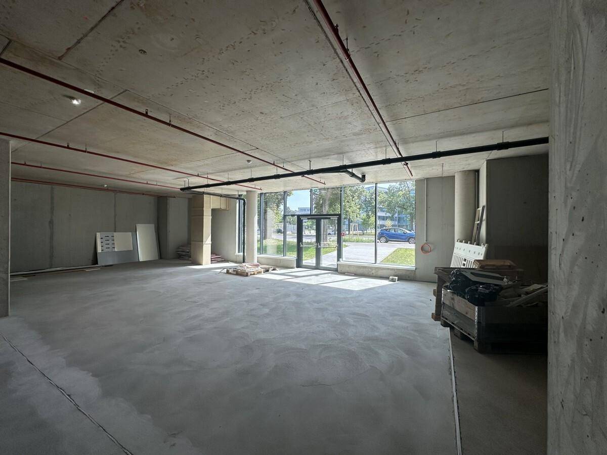 Ein weitläufiger, unfertiger Raum mit Betonboden, Säulen und großen Fenstern zur Straße.