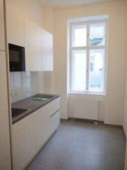 Moderne Küche mit weißen Schränken, dunkler Arbeitsplatte und einem Fenster für natürliches Licht.