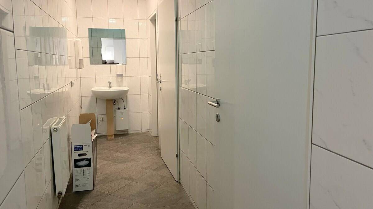 Modern gefliestes Badezimmer mit Waschbecken, Heizkörper und Spiegel, in heller Farbgebung.