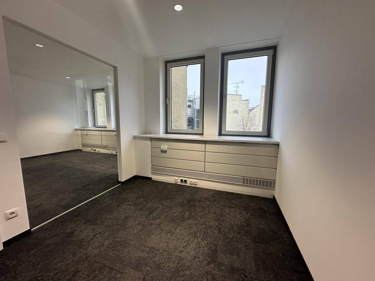 Geräumiges Büro mit Teppichboden, großen Fenstern und einer eleganten Glaswand, die den Raum unterteilt.