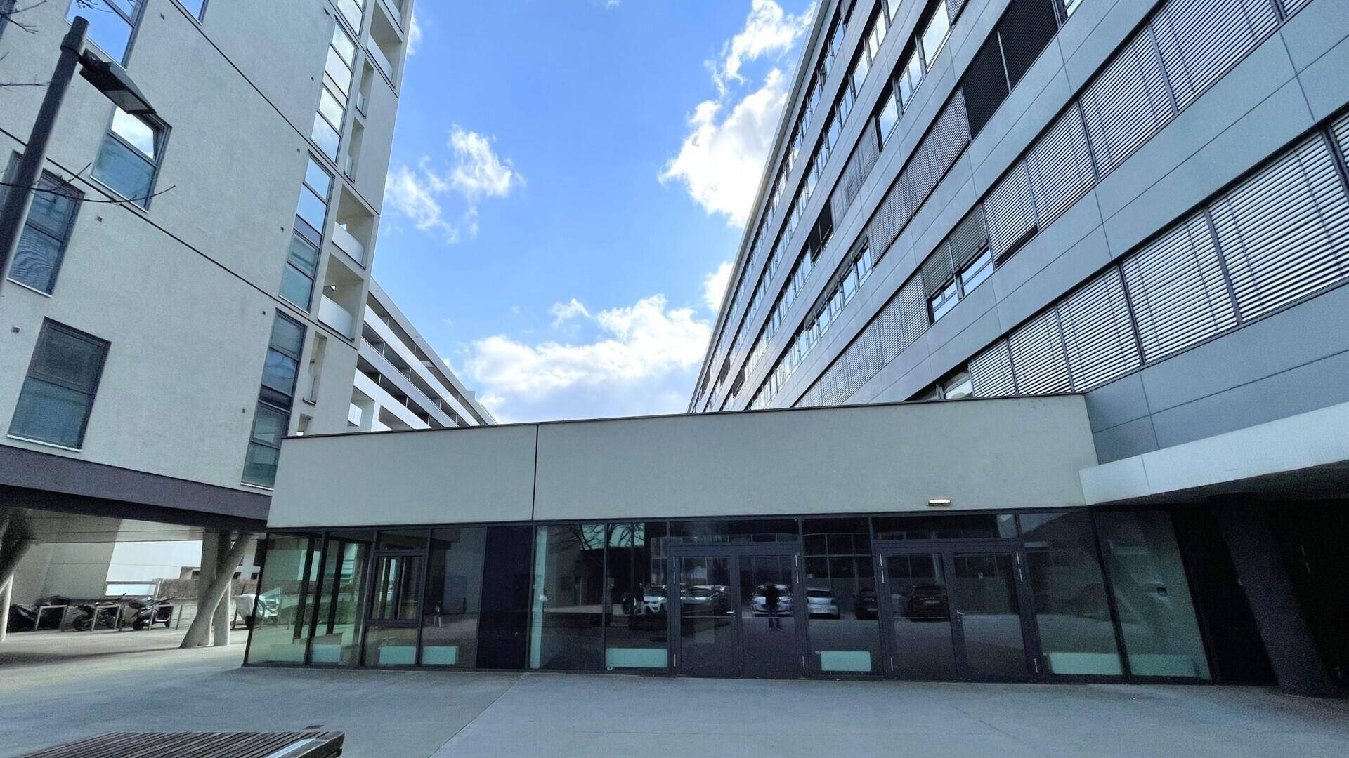 Ansicht eines modernen Geschäftsgebäudes mit großen Fensterfronten und einem weiteren Gebäude im Hintergrund.