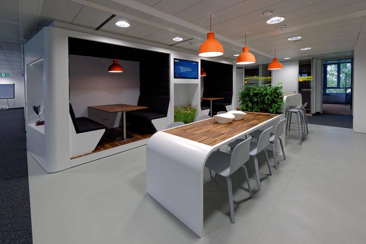Moderner Bürobereich mit flexiblen Arbeitsplätzen, Besprechungsnischen und stilvollen orangefarbenen Pendelleuchten.