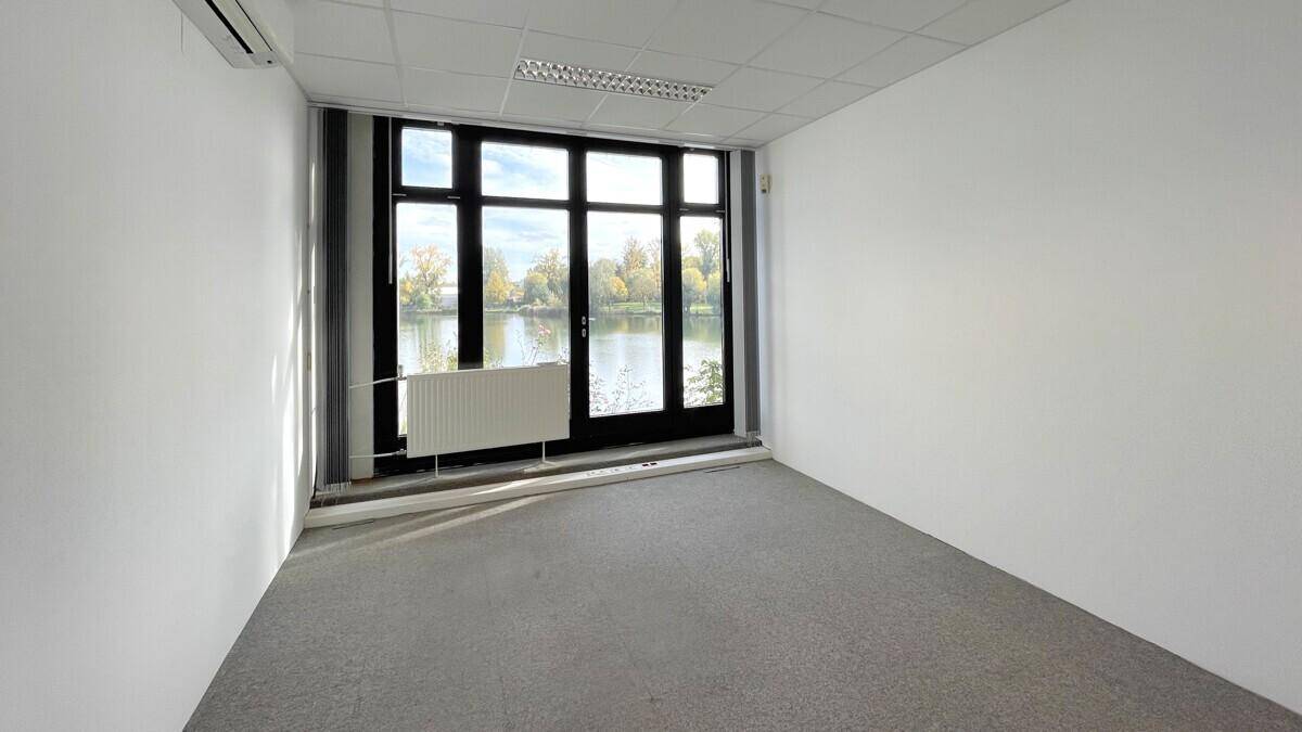 Leeres Büro mit Teppichboden und großem Fenster, das einen schönen Blick auf den See bietet.