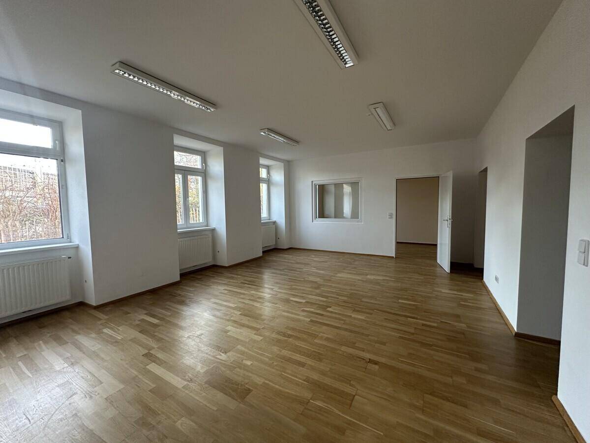 Geräumiger Büroraum mit Parkettboden, mehreren Fenstern und einer internen Fensteröffnung.