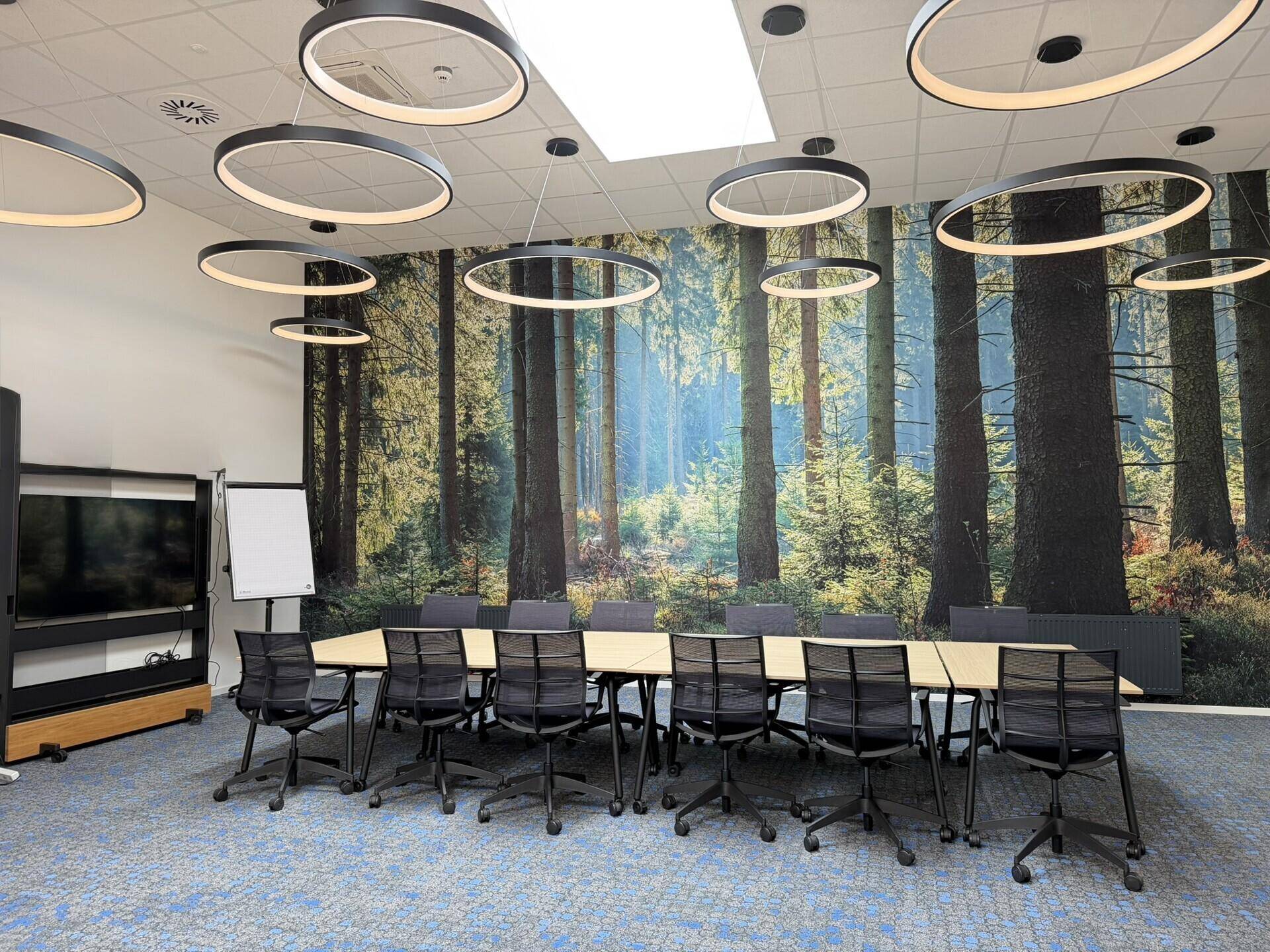 Moderner Konferenzraum mit großem Tisch, ergonomischen Stühlen und Waldmotiv-Tapete.