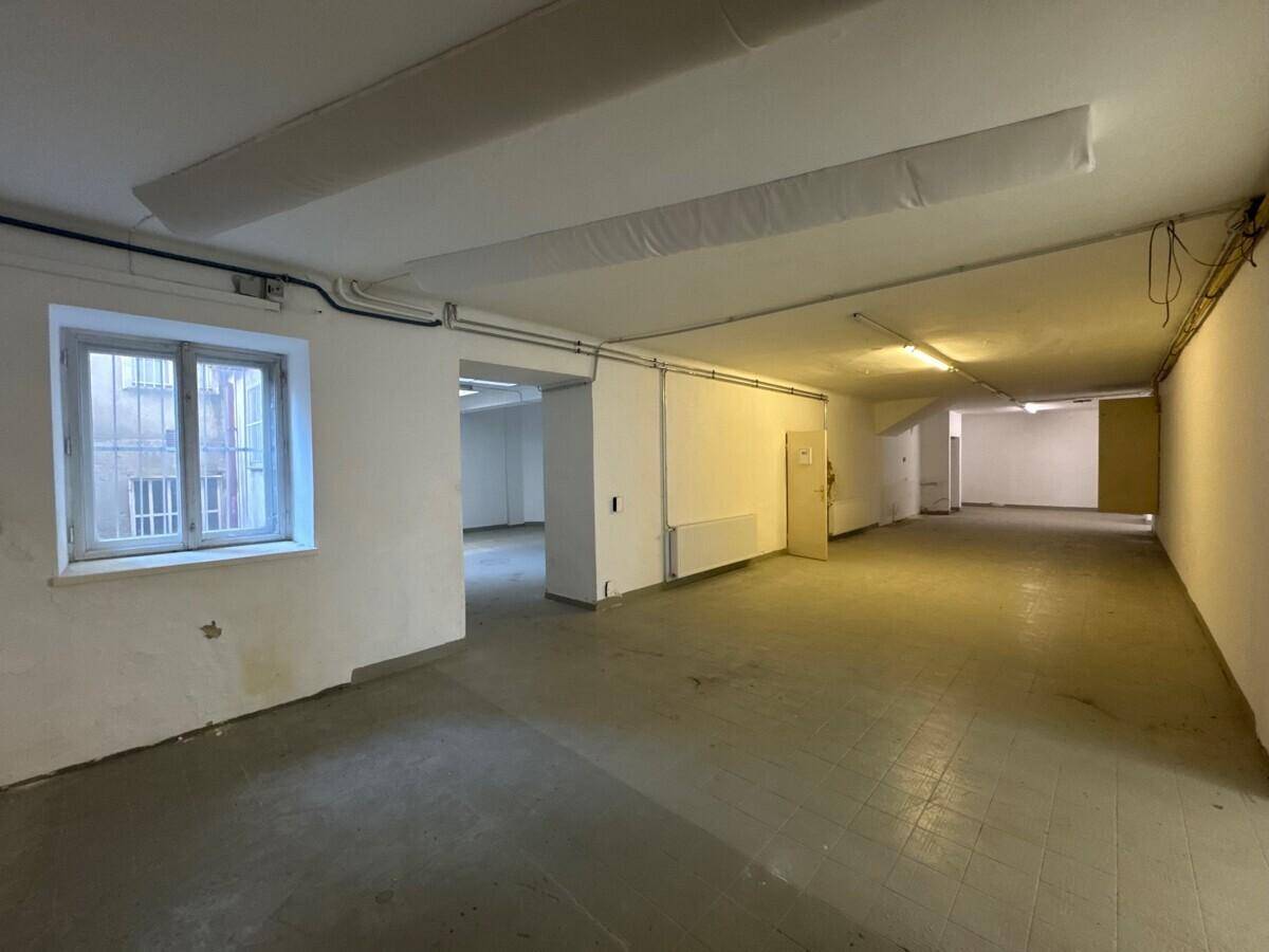 Langer Gewerberaum mit einem Fenster, sichtbaren Heizkörpern und einfacher Beleuchtung, bereit zur Gestaltung.