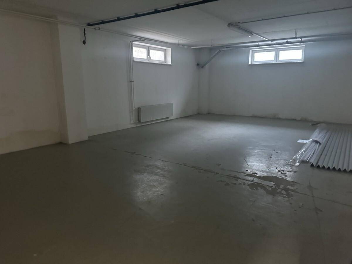 Geräumiger Kellerraum mit Betonboden, kleinen Fenstern und sichtbaren Leitungen an der Decke, ideal als Lagerfläche.