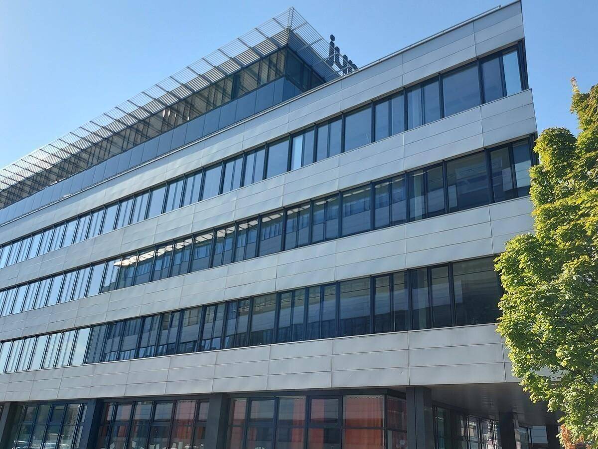 Detailansicht der modernen Bürogebäude-Fassade mit vielen Fenstern und horizontalen Elementen unter blauem Himmel.
