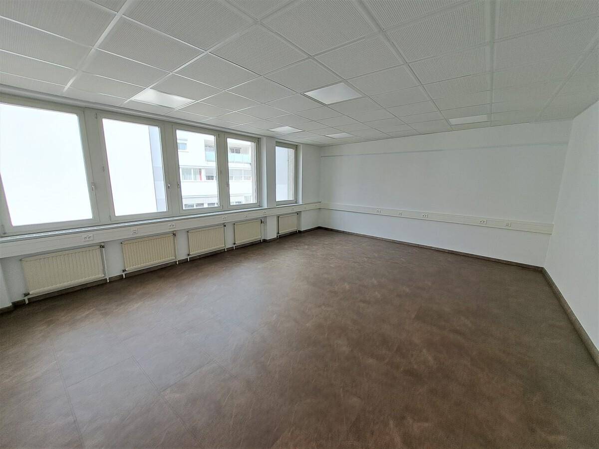 Heller Büroraum mit durchgehender Fensterfront und braunem Boden, ideal für flexible Arbeitsplatzgestaltung.