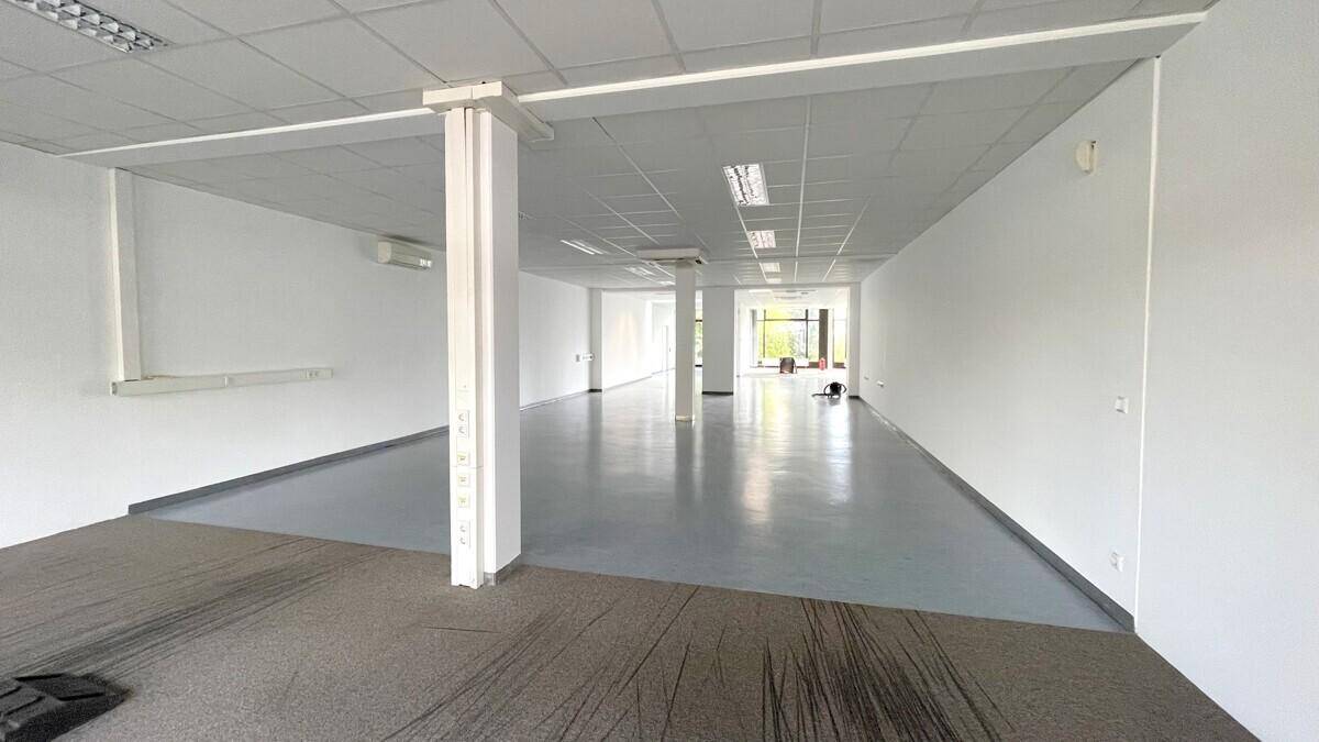 Langer, offener Gewerberaum mit gemischtem Bodenbelag und Säulen, der vielseitige Nutzungsmöglichkeiten bietet.
