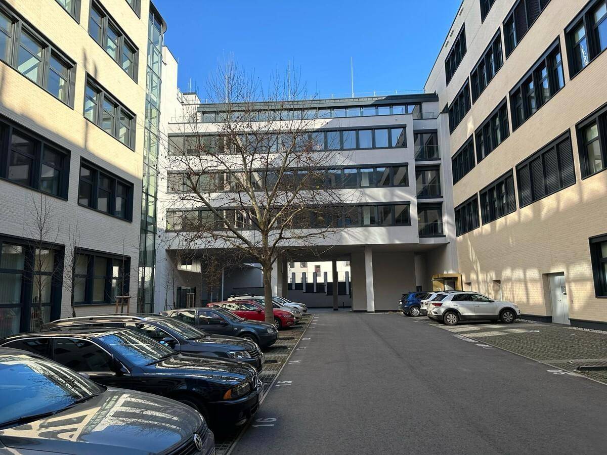 Innenhof eines Bürokomplexes mit zahlreichen Parkplätzen und modernen Gebäudefassaden unter blauem Himmel.