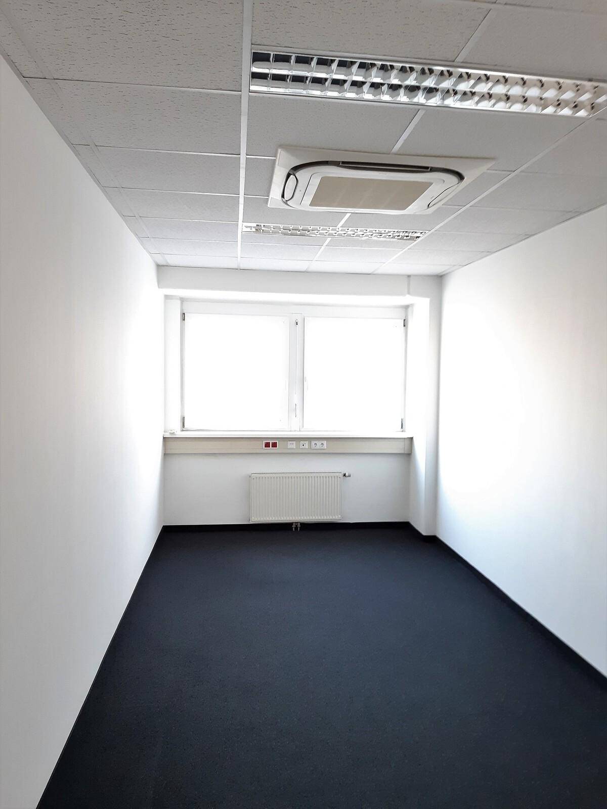 Leeres Büro mit dunklem Teppichboden, Deckenkassette und einer sichtbaren Klimaanlage, bereit zur Nutzung.