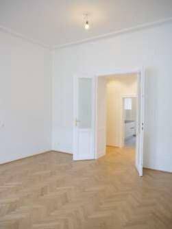 Geräumiges Zimmer mit Parkettboden und Doppeltüren, die zu einem weiteren Raum führen.
