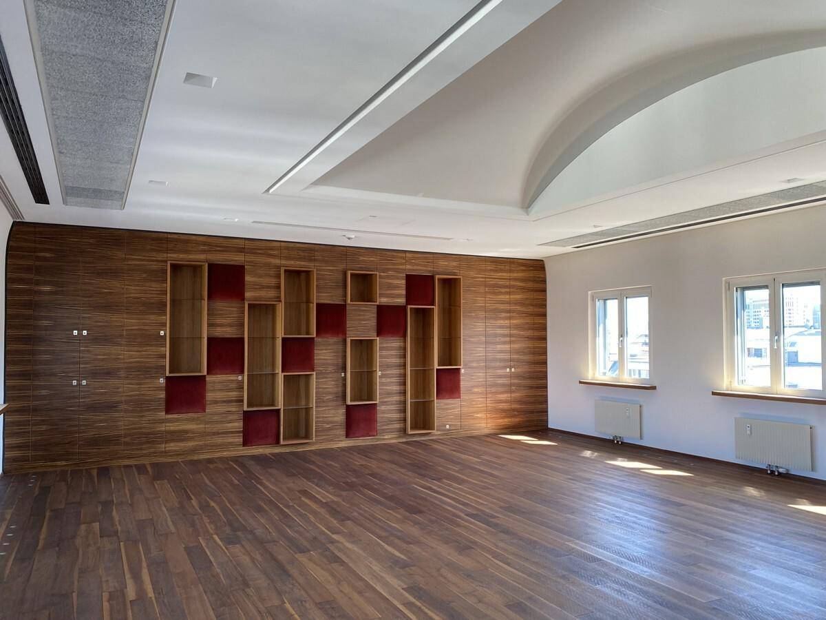 Großer Konferenzraum mit elegantem Holzboden, einer dekorativen Holzwand mit roten Akzenten und hohen Decken.