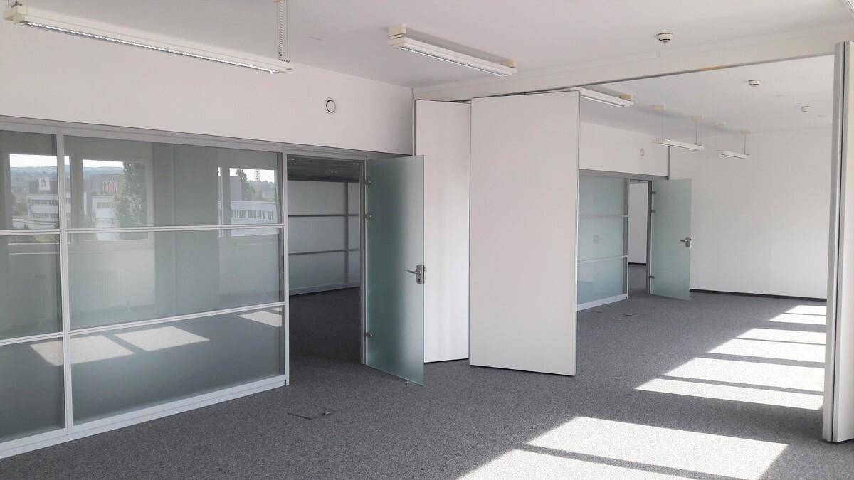 Geräumiger, leerer Büroraum mit Teppichboden und flexiblen Trennwänden aus Glas und undurchsichtigem Material.