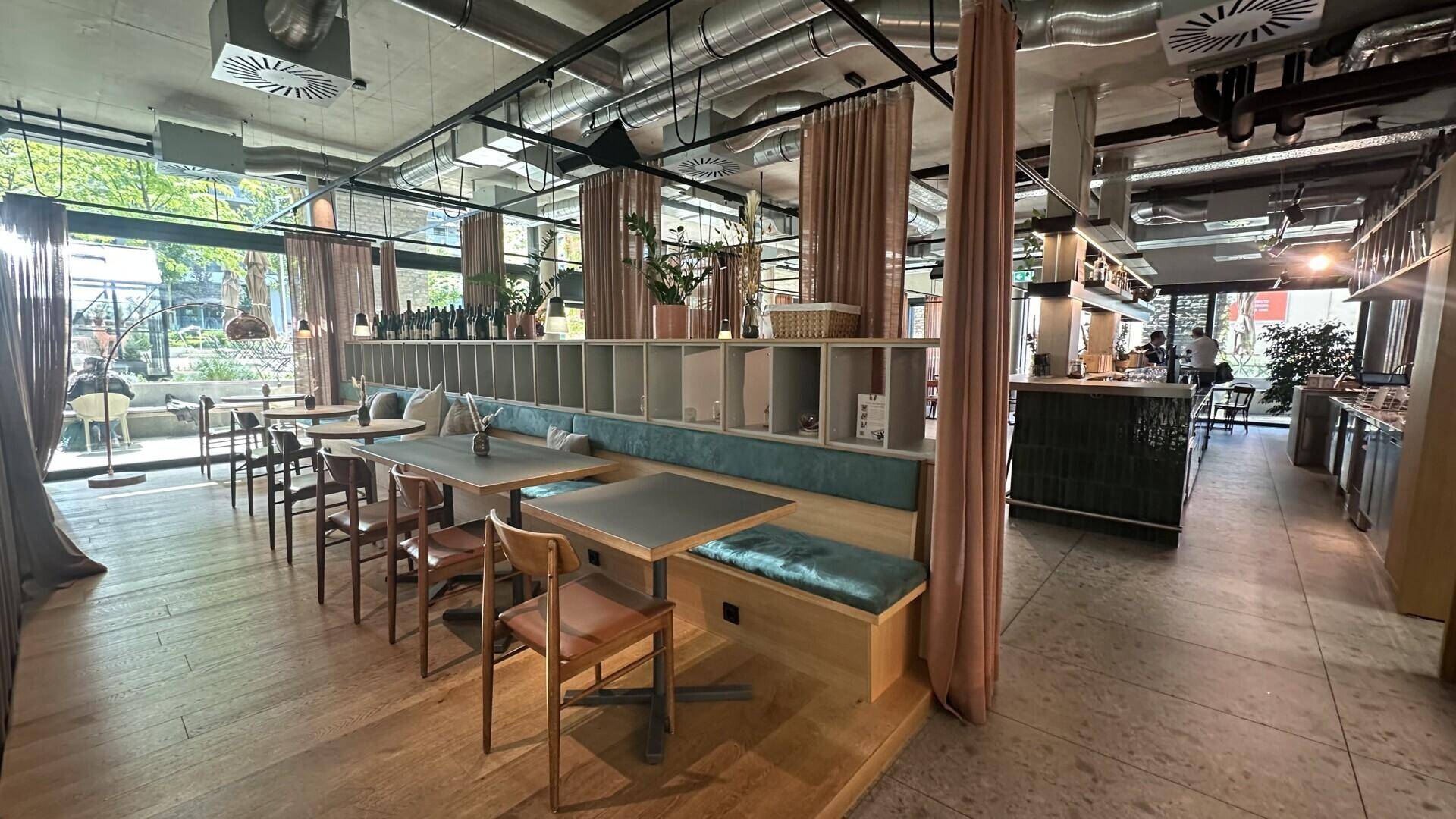 Gemütlicher Restaurantbereich mit Holztischen, Sitzbänken und großen Fenstern, unter einer modernen Deckenkonstruktion.