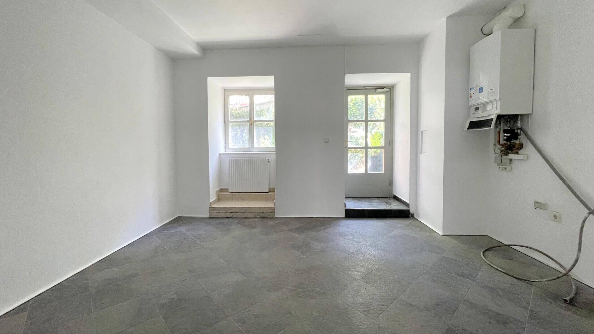Raum mit einem Warmwasserbereiter an der Wand, grauen Fliesen und Fenstern, möglicherweise ein Technikraum.