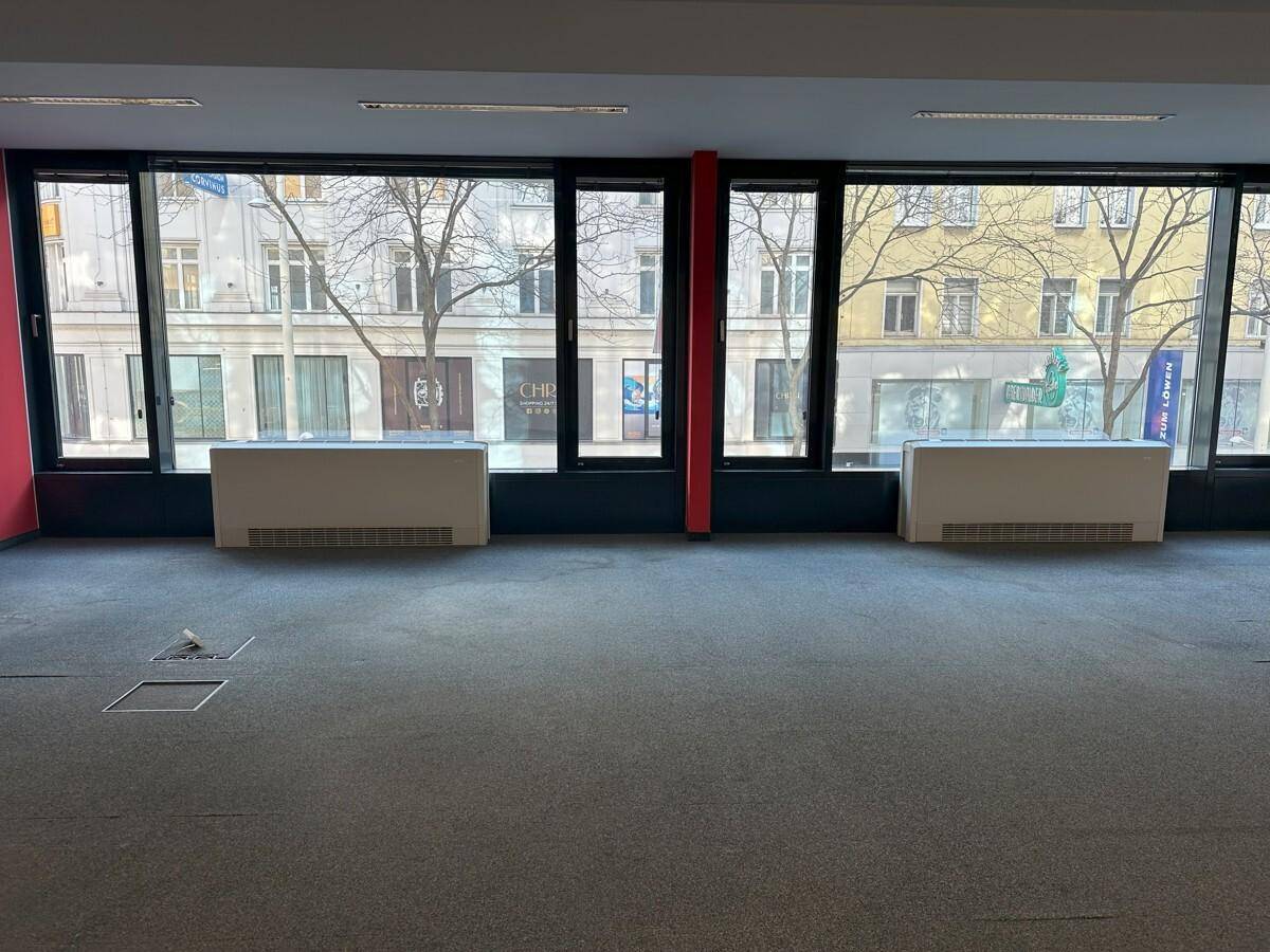 Innenraum mit großen Fenstern, die einen direkten Blick auf die belebte Stadtstraße und umliegende Gebäude ermöglichen.
