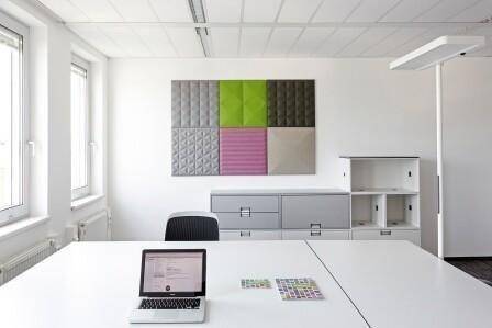 Modern eingerichtetes Büro mit Schreibtisch, Laptop und farbigen Akustikpaneelen an der Wand.