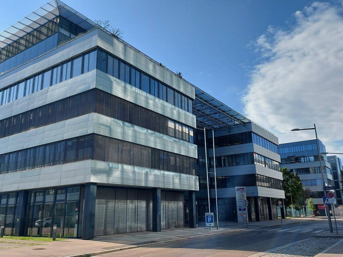 Ansicht mehrerer moderner Bürogebäude mit reflektierenden Glasfassaden und Jalousien, an einem sonnigen Tag.