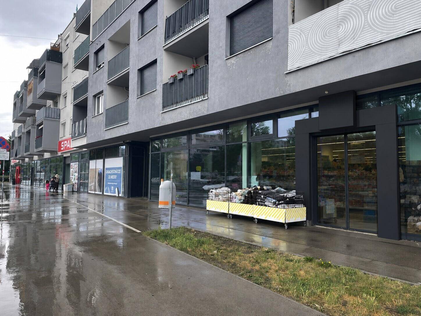 Ansicht der modernen Geschäftsfronten und Wohnungen an einer nassen Straße nach einem Regenschauer.