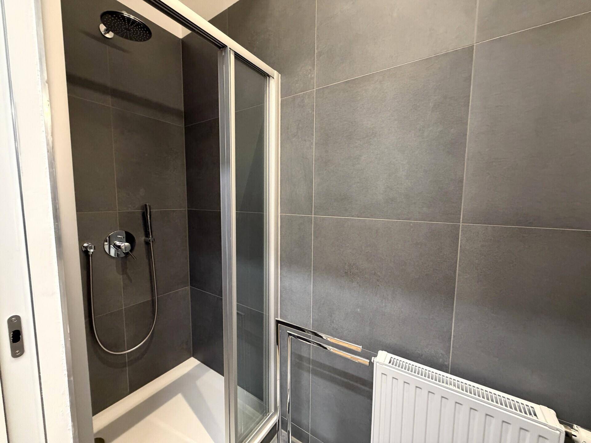 Modernes Badezimmer mit dunklen Fliesen, Duschkabine und Regendusche.