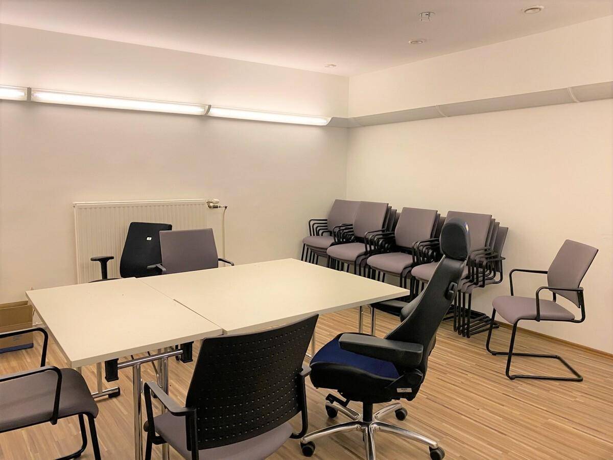 Heller Konferenzraum mit Tischen und Stühlen, ideal für Besprechungen oder Schulungen.