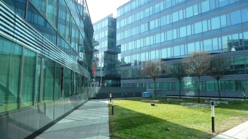 Moderner Bürokomplex mit reflektierenden Glasfassaden, umgeben von gepflegten Grünflächen und Bäumen.
