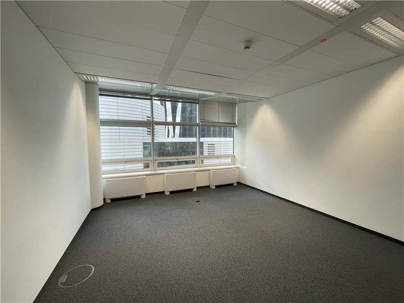 Leeres Büro mit Teppichboden und einer Fensterfront, die ausreichend Tageslicht für einen Arbeitsplatz bietet.