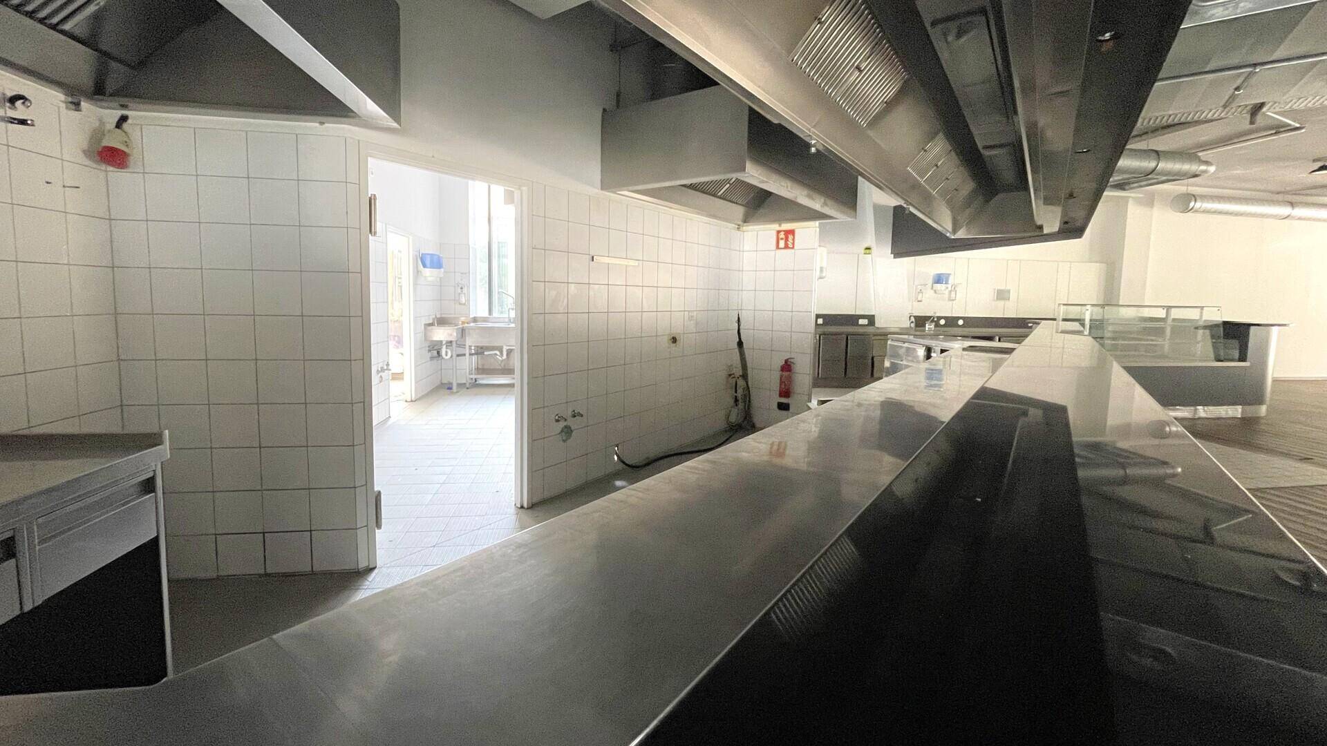 Große Gewerbeküche mit gefliesten Wänden, Edelstahlarbeitsflächen und professionellen Dunstabzugshauben.