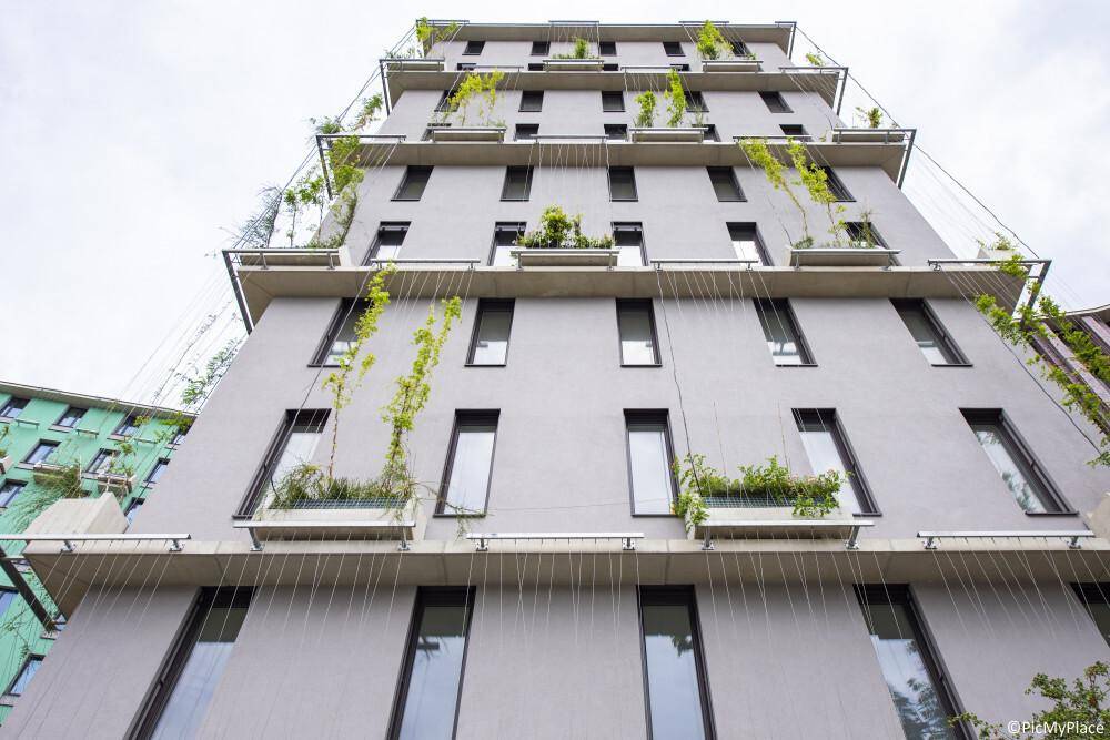 Moderne Gebäudefassade mit vertikalen Begrünungselementen und vielen Fenstern unter hellem Himmel.