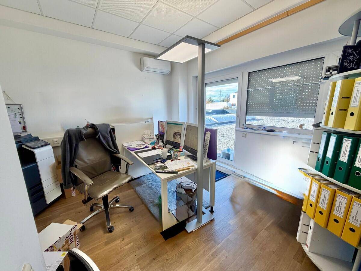 Helles Einzelbüro mit Holzboden, Schreibtisch, Bürostuhl und einem Fenster mit Blick nach draußen.