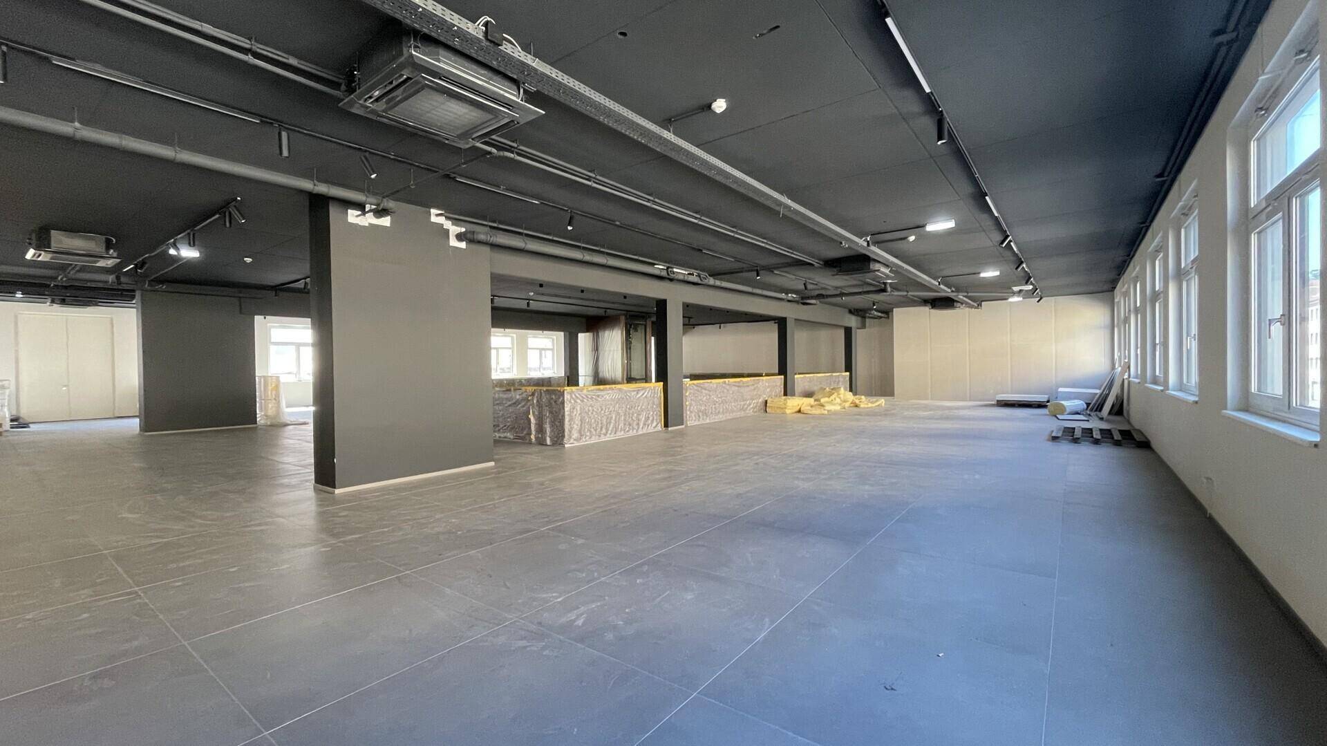 Weitläufiger Bürobereich mit dunkler Decke, vielen Fenstern und industriellem Charme.