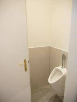 Separate Toilette mit Urinal und hellen Fliesen, sichtbar durch eine offene Tür.