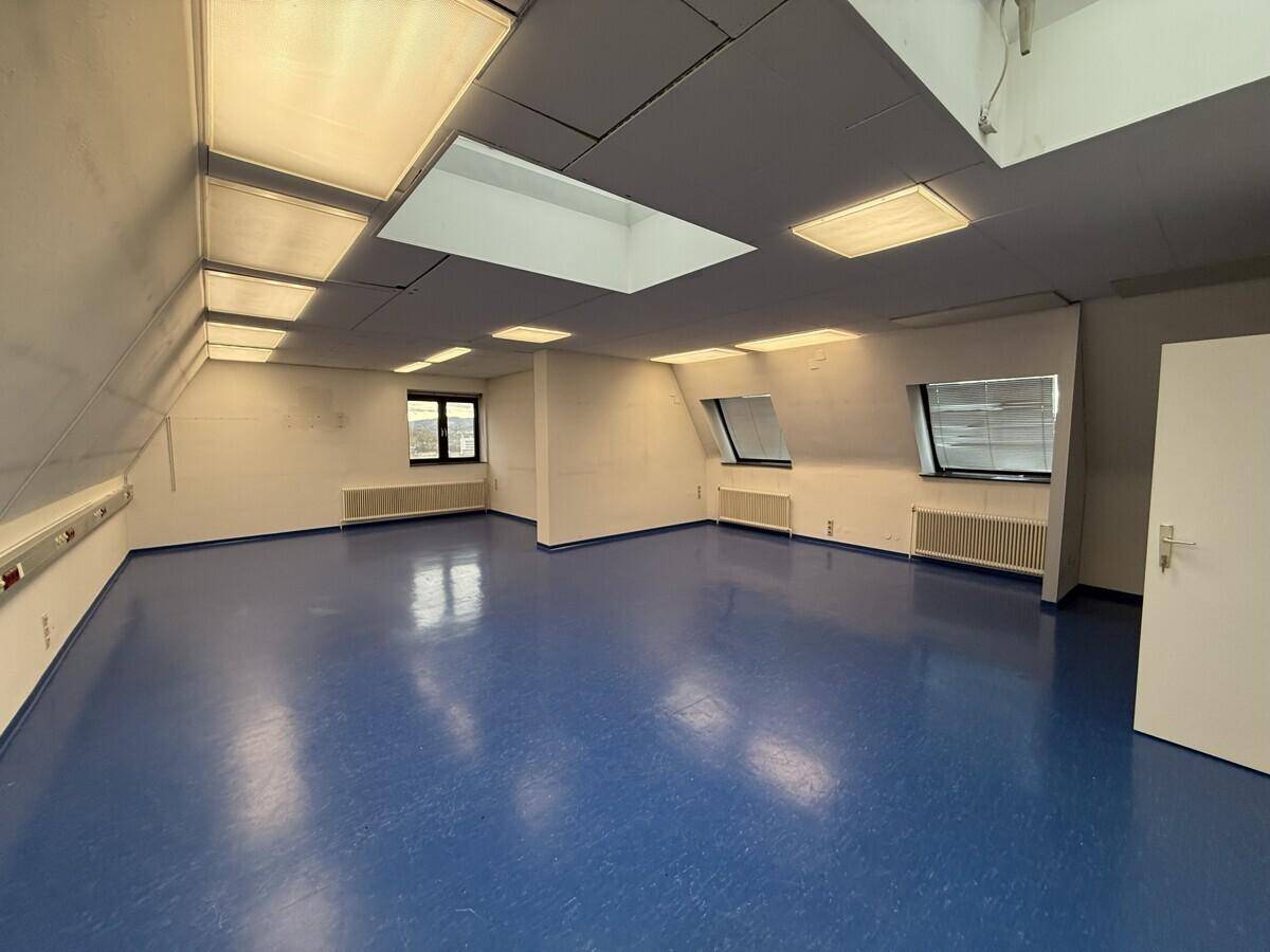 Großer, leerer Büroraum im Dachgeschoss mit blauen Vinylböden und Dachfenstern, bereit zur individuellen Gestaltung.