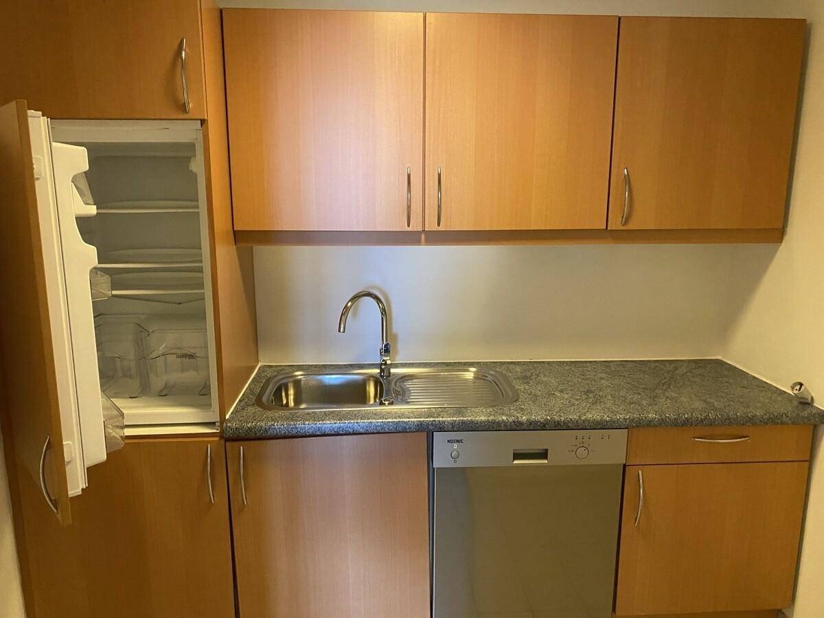Funktionale Küchenzeile mit Holzschränken, grauer Arbeitsplatte und integriertem Kühlschrank.