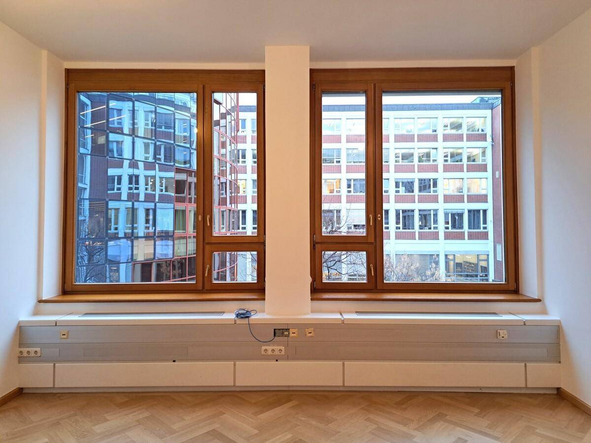 Geräumiger Büroraum mit Holzfenstern, Parkettboden und viel Tageslicht.