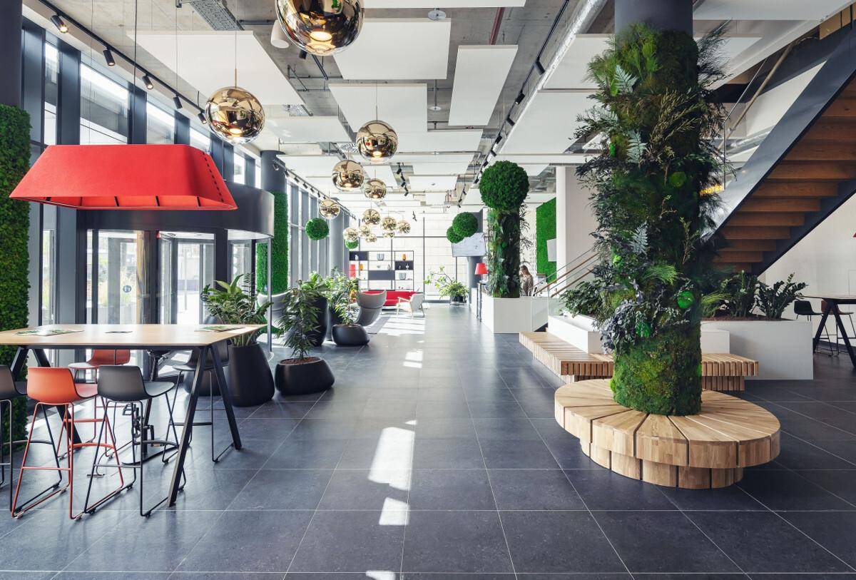 Geräumige, moderne Lobby mit hohen Decken, dunklen Fliesen und üppiger Begrünung als Gestaltungselement.
