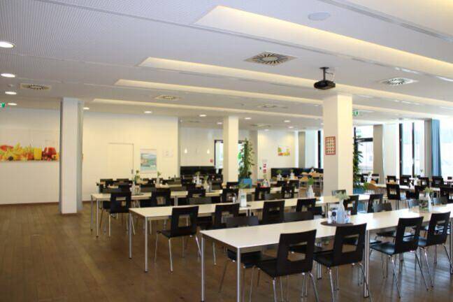 Geräumige Cafeteria mit vielen Tischen und Stühlen, ideal für Mitarbeitermahlzeiten und Pausen.