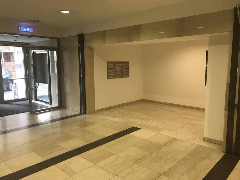 Heller Eingangsbereich mit beigefarbenen Fliesen, einer Glastür und Briefkästen an der Wand.
