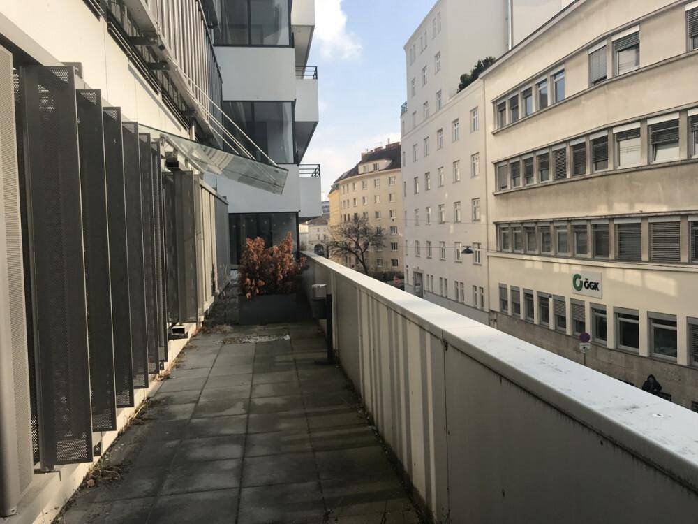 Langer Balkon mit Blick auf die umliegenden Gebäude und eine städtische Umgebung, mit Fliesenboden.