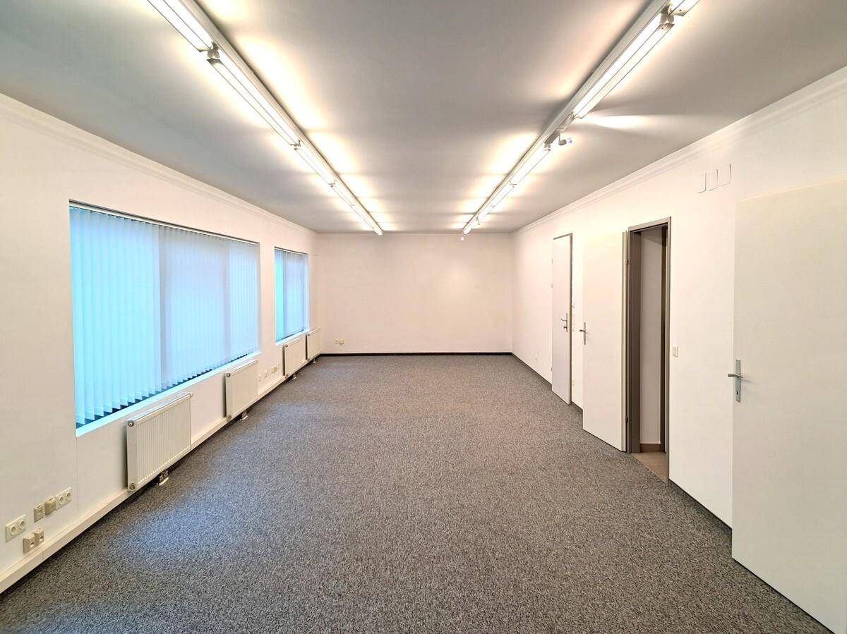 Geräumiger, leerer Büroraum mit Teppichboden, mehreren Fenstern und effizienter Deckenbeleuchtung.