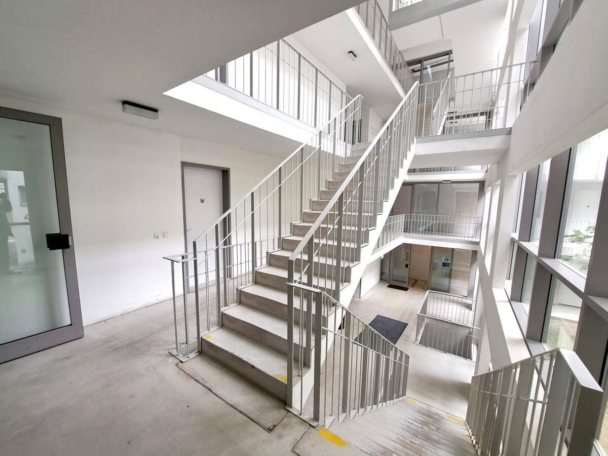 Modernes Treppenhaus mit mehreren Etagen, Metallgeländern und viel Tageslicht durch große Fenster.
