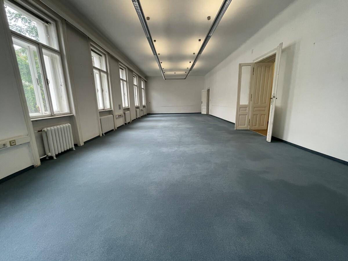 Großer, langer Büroraum mit vielen Fenstern, blauem Teppichboden und moderner Deckenbeleuchtung.
