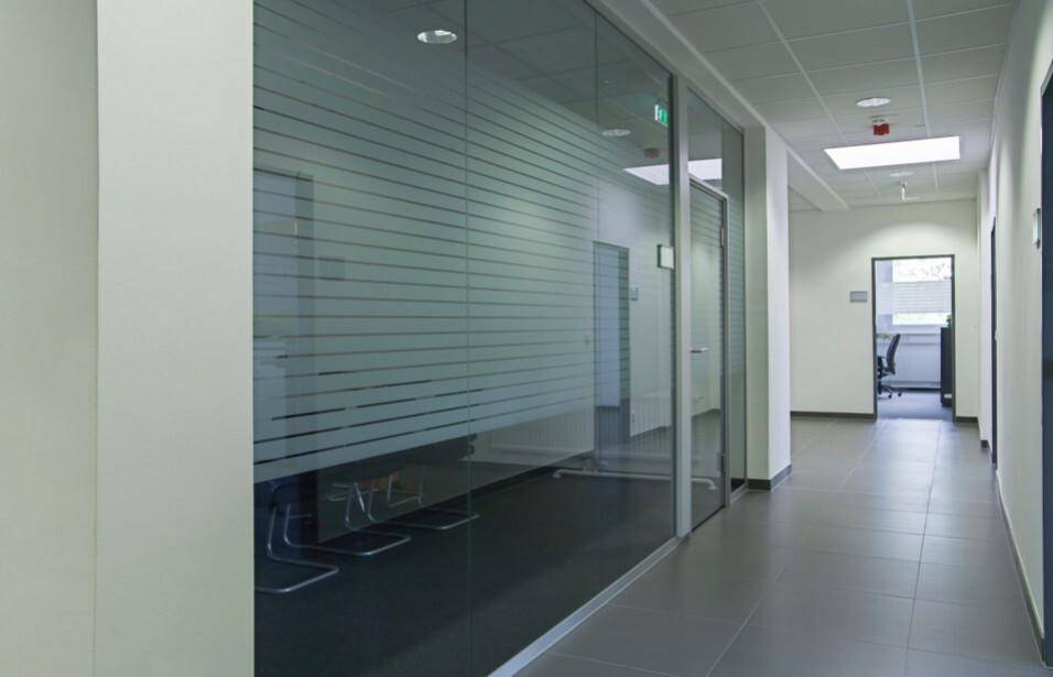 Bürogang mit Glaswänden, teilweise satiniert, der zu weiteren Räumen führt, mit Fliesenboden.