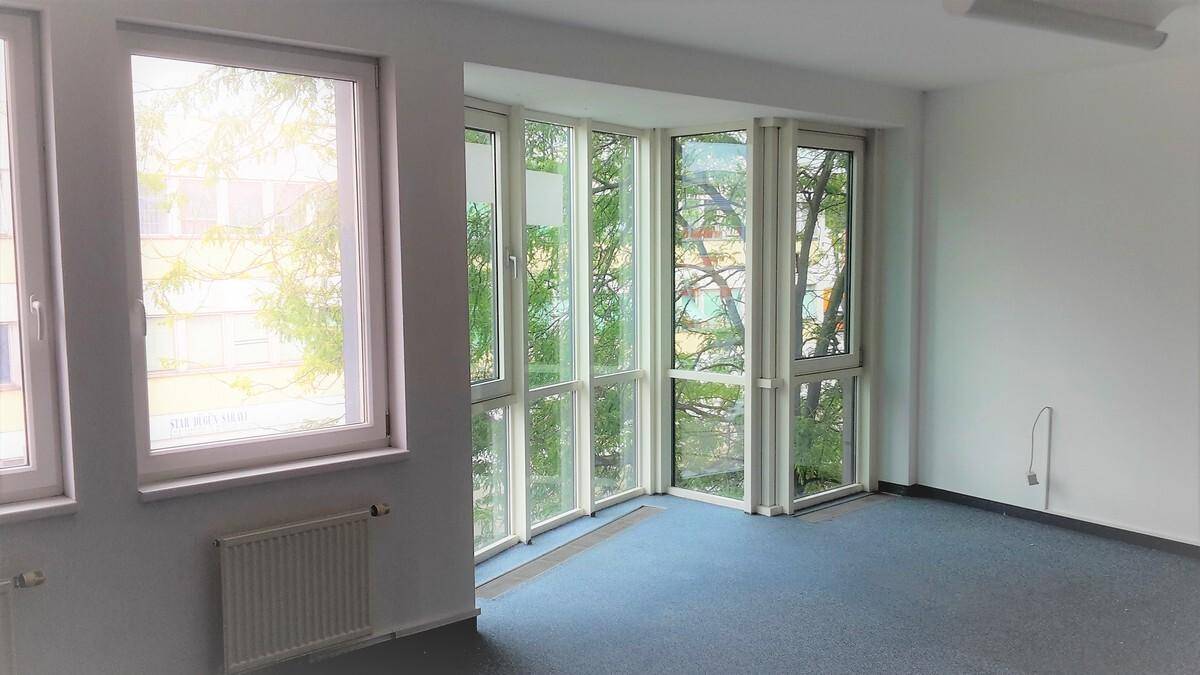 Leeres Büro mit großen Fenstern, blauem Teppichboden und Heizkörpern unter den Fenstern.