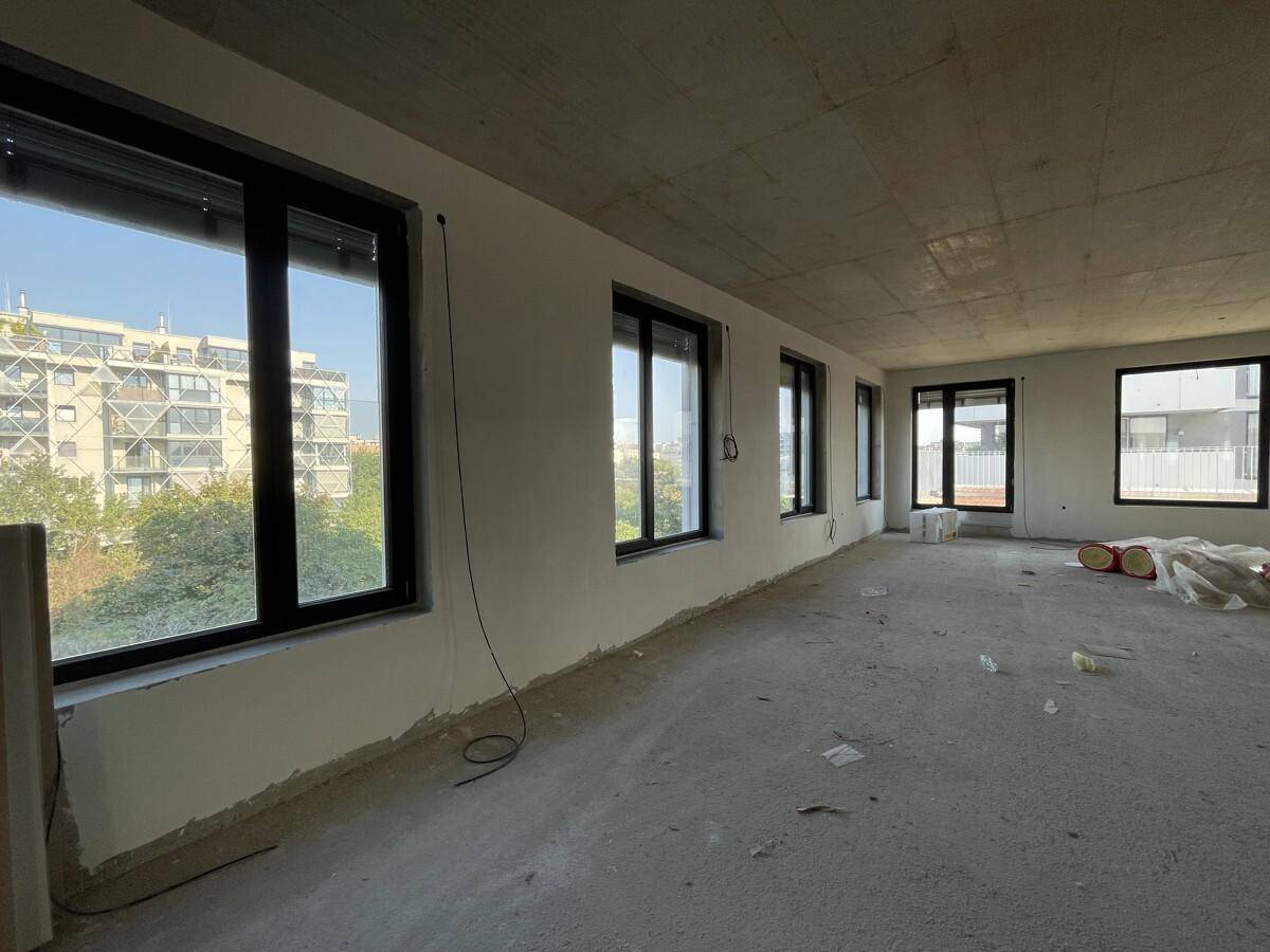 Unfertiger Büroraum mit Betonboden und -decke, großen Fenstern und Blick auf die Stadt.