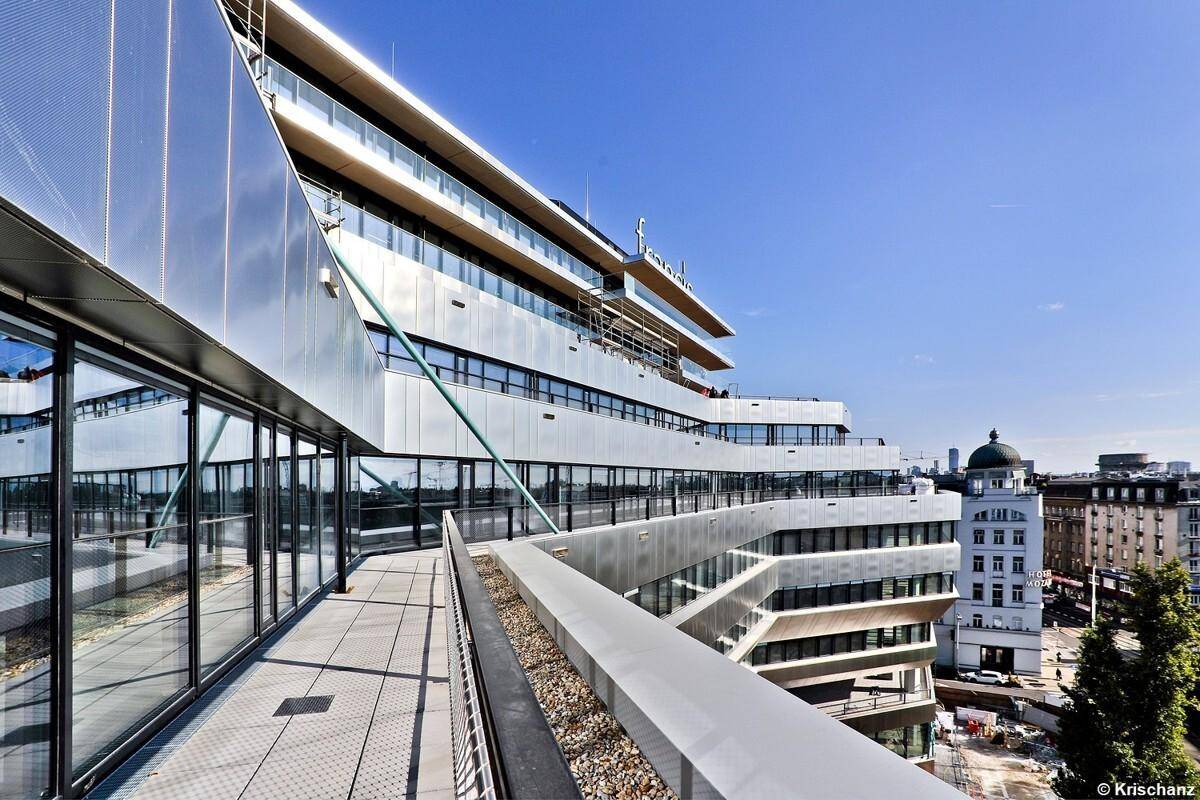 Die geschwungene Fassade des modernen Gebäudes mit einer langen Terrasse und Blick auf die Stadt.