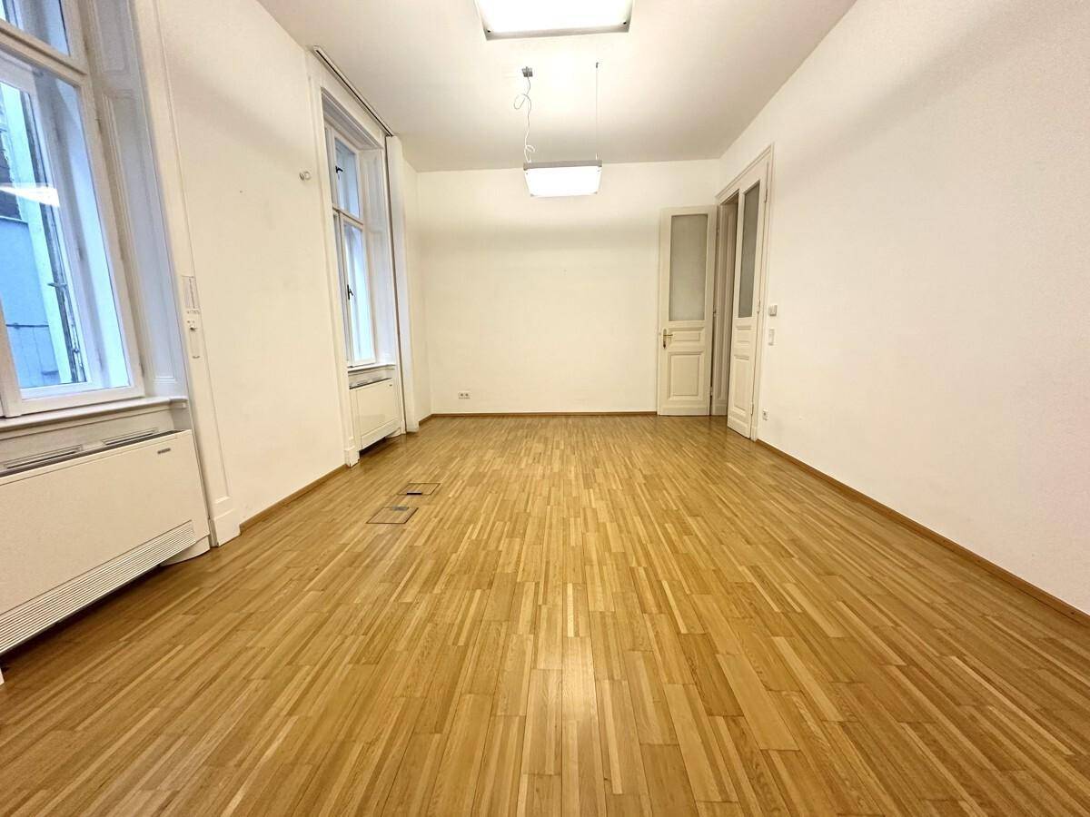 Heller Büroraum mit Holzboden, hohen Fenstern und weiß gestrichenen Wänden.
